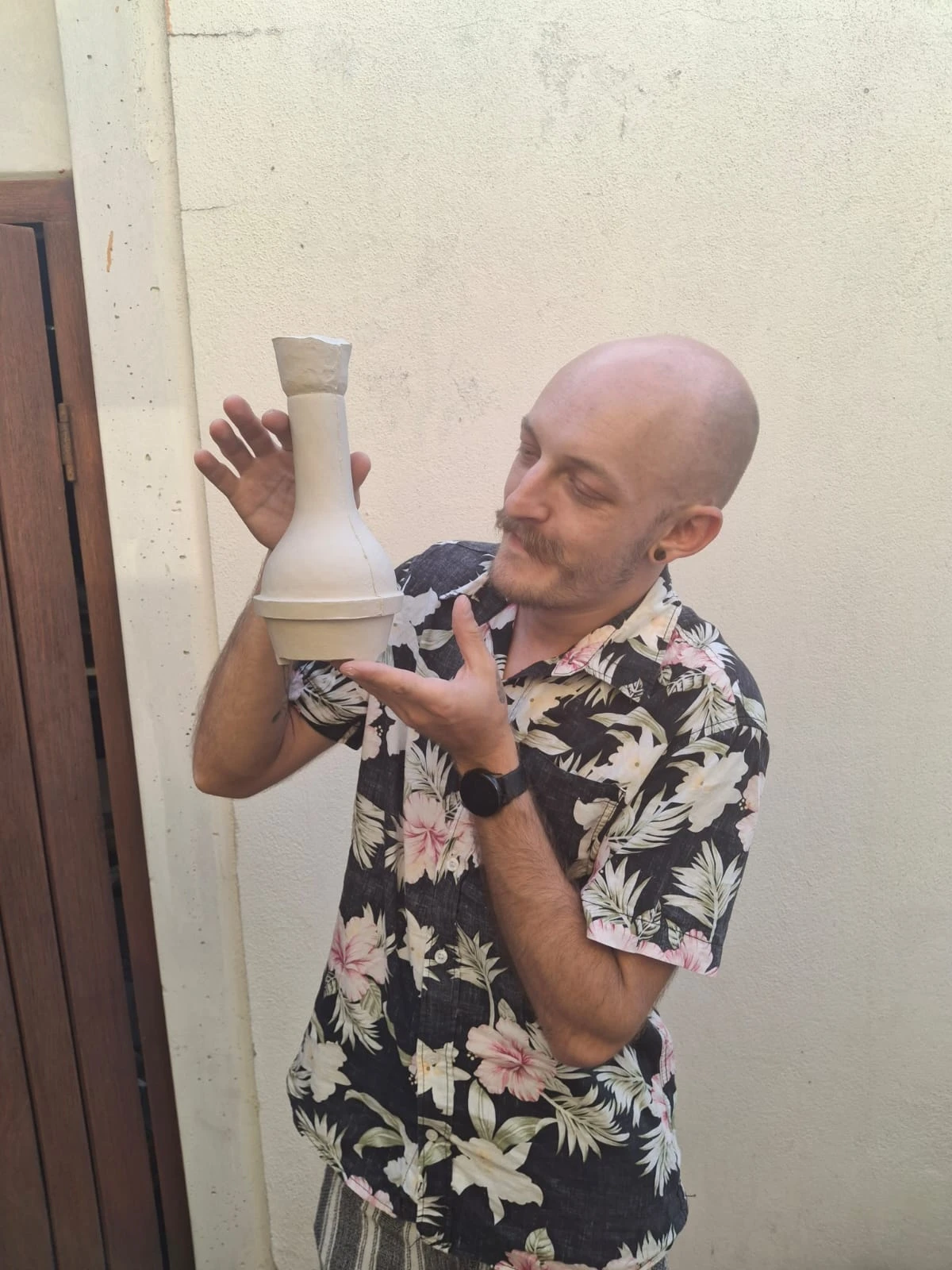Johan in a floral shirt, admiring an unglazed Fynbongs piece he holds up in his hands